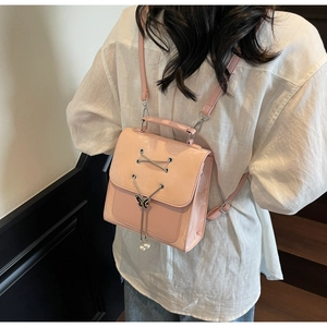 Detail of pink patent leather backpack featuring a butterfly charm and pearl accents