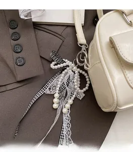 Detail of elegant pearl bow charm with lace ribbon and lobster clasp on handbag