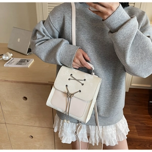 Détail d'un sac à dos crème avec laçage croisé, papillon en métal et perles décoratives