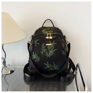 Detail of black backpack with green leaf pattern, gold brand plate and metal zippers