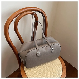 Close-up of grey leather boston bag with long straps on a classic woven chair