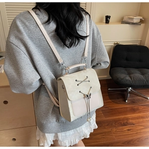 Detail of cream PU leather backpack featuring lace-up design and pearl butterfly pendant