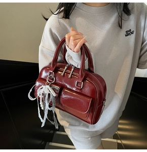 Detail of dark red Boston bag with glossy finish and decorative pearl lace pendant