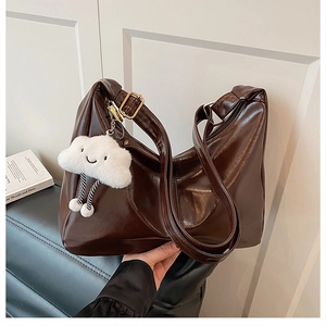 Detail of dark brown hobo bag in glossy leather with plush white cloud charm and gold buckle