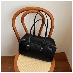 Detail of black pebbled leather Boston bag with long handles on a designer wooden chair