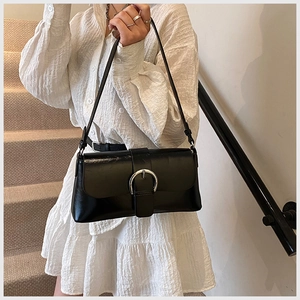 Close-up of a glossy black retro shoulder bag with a large silver metal buckle on the flap