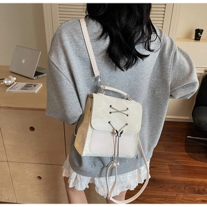Détail d'un mini sac à dos crème avec laçage et breloque papillon perlé porté par un mannequin