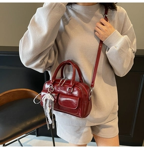 Detail of burgundy glossy leather Boston bag with decorative pockets and bow charm