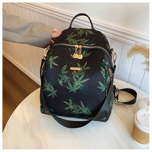 Detail of waterproof nylon backpack with green leaf print and golden zippers on white table