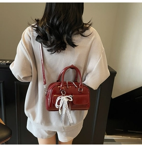 Detail of dark red patent leather Boston bag with lace bow on model back view