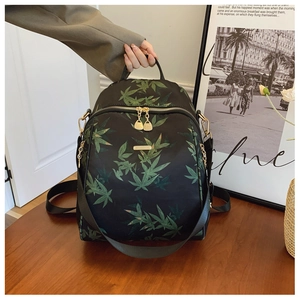 Detailed close-up of a black backpack with green maple leaf pattern and gold metal logo