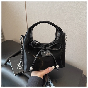 Détail du sac en cuir verni noir avec un grand nœud et une plaque en métal argenté poli