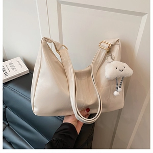 Detail of creamy white leather tote bag featuring gold hardware and soft cloud pendant