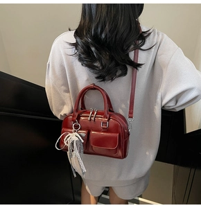Detail view of burgundy leather Boston bag featuring pearl charm and twin front pockets