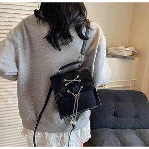 Détail d'un sac à bandoulière noir brillant avec fermoir papillon et breloque en perles