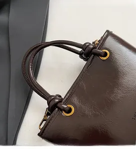 Détail du sac seau en cuir verni marron foncé avec poignée tressée et accents dorés