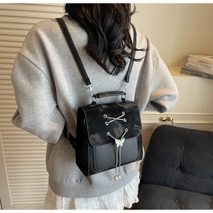 Détail du sac à dos noir avec rabat marbré, sangles croisées et boucle papillon en perles
