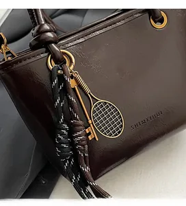 Détail d'un sac en cuir ciré marron foncé avec charms en métal et cordons tressés