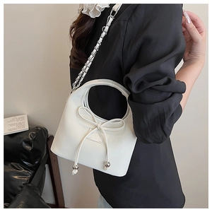Détail du sac bandoulière crème avec nœud en cuir et bandoulière chaîne argentée