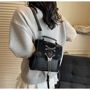 Detail of a black mini backpack featuring a metal lace-up design and pearl butterfly charm