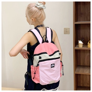 Side view of a woman wearing a pink and beige color-block nylon backpack with side pockets