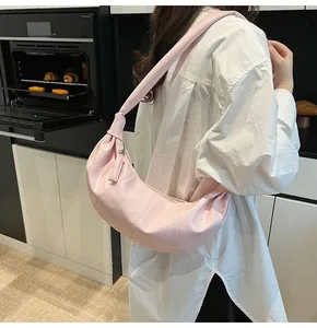 Detail view of pink pleated crescent bag with glossy finish on a shoulder-worn model