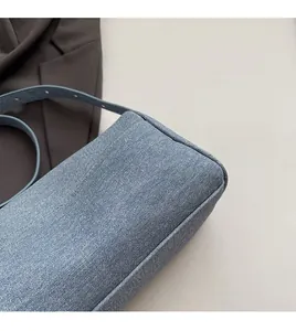 Detail of light blue denim fabric texture and reinforced piping on a small crossbody bag