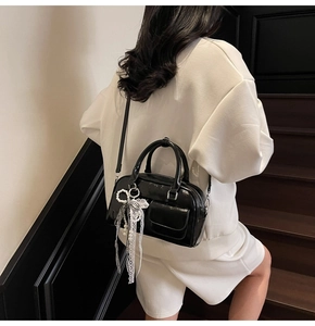 Close-up of black Boston bag with lace pearl bow and glossy patent leather detail