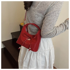 Gros plan d'un sac bandoulière en cuir verni rouge avec nœud et bandoulière en chaîne