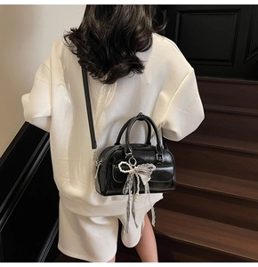 Detail of black Boston bag featuring a checkered bow and pearl pendant with top handles