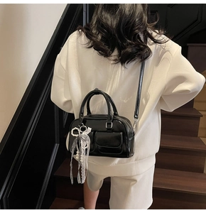 Rear view of black leather Boston bag with pearl bow charm on model against wooden stairs