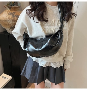 Model wearing a black glossy croissant bag showing its stylish half-moon shape and size