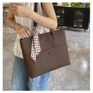 Detail of a large brown leather tote bag with houndstooth scarf and front buckle pocket