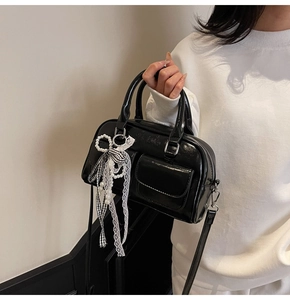 Close-up of black Boston bag with glossy finish and pearl bow charm detail