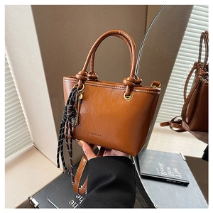 Vue détaillée du sac seau en cuir marron avec poignées nouées et breloque en corde
