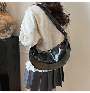 Detailed view of black glossy crescent bag with vertical stitching and wide strap