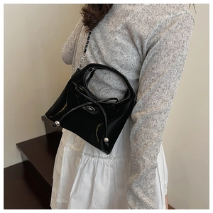 Détail du sac bandoulière en cuir verni noir avec un nœud et des boules métalliques