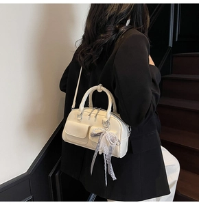 Chic cream Boston bag with pearl bow charm shown on model in urban fashion setting