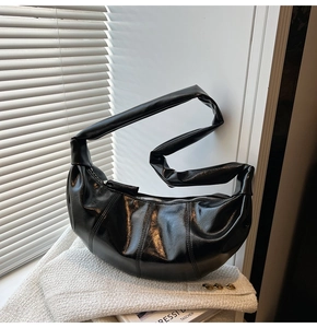 Detail of black glossy pleated dumpling bag with padded strap on a white tweed jacket