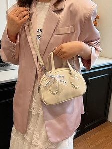 Chic beige lychee leather crossbody bag with decorative ribbon shown on model in soft lighting