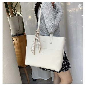 Close-up of a white lychee leather tote bag with silk scarf detail and brand logo