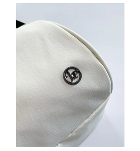 Close-up of white ripstop fabric texture and metallic logo detail on a shell shoulder bag