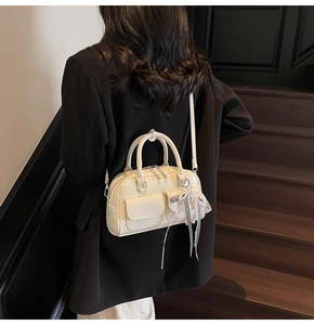 Detail of off-white leather Boston bag with decorative plaid bow and lace charms