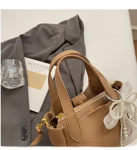 Close-up of brown pebbled leather bucket bag with lace bow charm on grey blazer