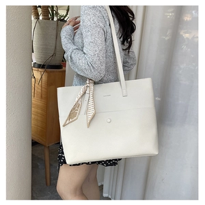 Close-up of beige leather tote bag with silk scarf detail in a home interior setting