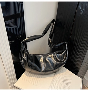 Detail of glossy black hobo bag with wide knotted strap and vertical stitching accents