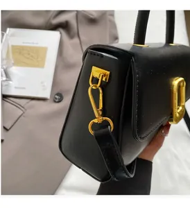 Gros plan sur un sac à main carré noir mat avec des détails en métal doré épais