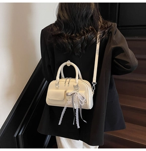 Detail of cream Boston bag with pearl lace bow charm worn over a black blazer