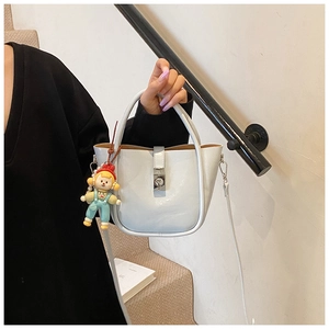 Macro view of cream bucket bag with silver buckle, leather handle and cute doll charm