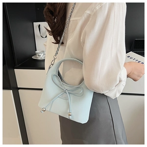 Détail du sac à bandoulière bleu clair avec nœud géant et sangle en chaîne sur le modèle